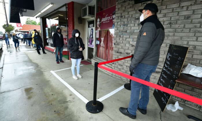 Observando las pautas de distanciamiento social, el dueño de una tienda se reúne con los clientes haciendo fila en Whittier, California, el 9 de abril de 2020. (Frederic J. Brown/AFP/Getty Images)