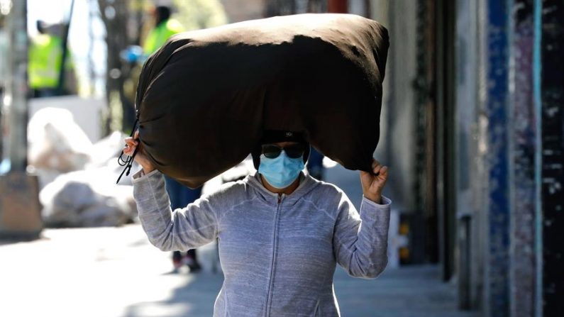 Una mujer usa una máscara facial de protección mientras lleva un saco en la cabeza en el Bronx. (Nueva York, EE.UU.) EFE/Peter Foley
