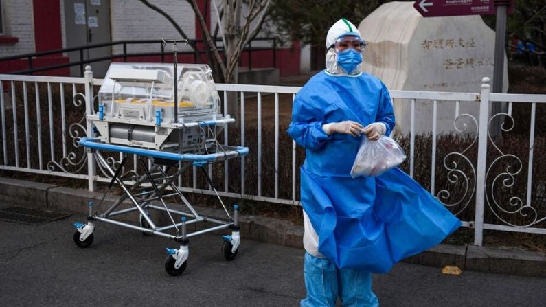 Un trabajador médico usa ropa de protección como medida preventiva contra el virus del PCCh mientras espera a que un guardia de seguridad abra una puerta antes de mover una incubadora entre edificios en un hospital de Beijing el 21 de febrero de 2020. (GREG BAKER/AFP vía Getty Images)