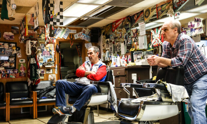 Los barberos y hermanos Tommy (izq.) y Jimmy Checkler ven las últimas noticias sobre el coronavirus en su barbería vacía de la ciudad de Worthington en Columbus, Ohio, el 17 de marzo de 2020. (Charlotte Cuthbertson/The Epoch Times)