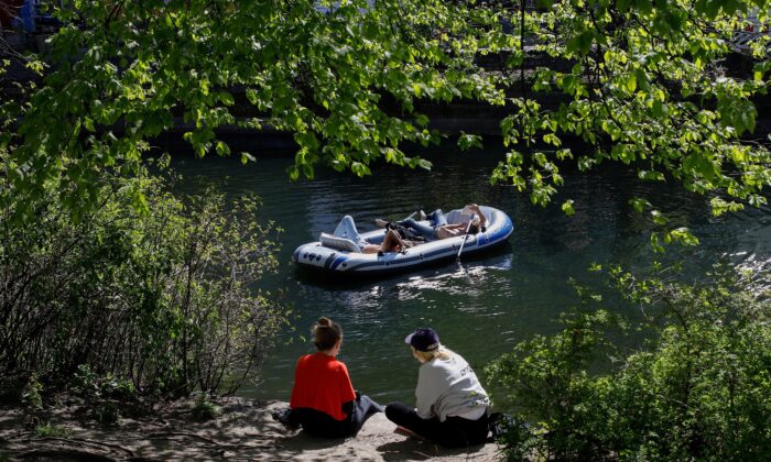 La gente se sienta al sol mientras otros se relajan en un bote inflable a lo largo del canal Landwehr en el distrito Kreuzberg de Berlín el 18 de abril de 2020. (David Gannon/AFP vía Getty Images)