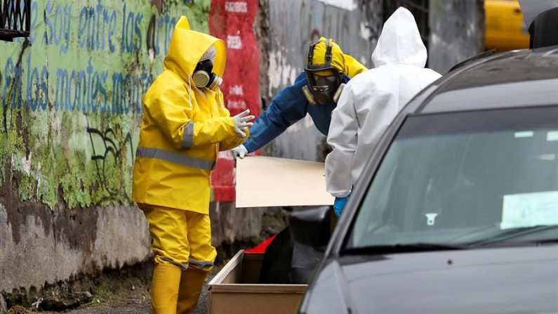 QUITO (ECUADOR), 05/05/2020.- Miembros de una funeraria, vestidos con trajes especiales como medida de protección contra la COVID-19, embalan con plástico una caja de madera donde se encuentra el cuerpo de un adulto de 65 años que falleció este martes en una calle de Quito (Ecuador). EFE/ José Jácome
