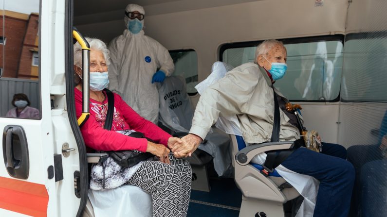 Dos ancianos infectados con COVID-19 se toman de la mano mientras son transportados por voluntarios de la Cruz Roja  a otra residencia donde solo hay infectados con el virus del PCCh, el 28 de abril de 2020. (Alvaro Calvo/Getty Images)