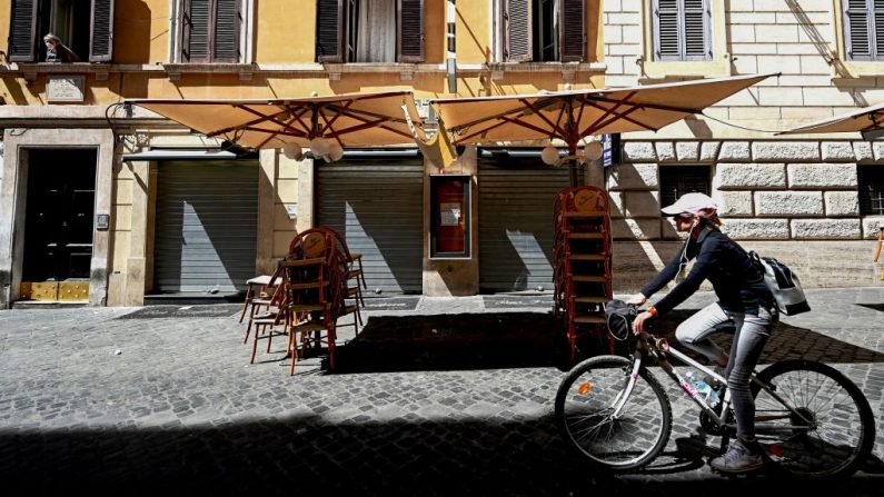 Una mujer pasa en bicicleta por un café cerrado en el centro de Roma (Italia) el 8 de mayo de 2020, durante el cierre del país para frenar la propagación de la infección COVID-19, causada por el virus del PCCh. (VINCENZO PINTO/AFP vía Getty Images)