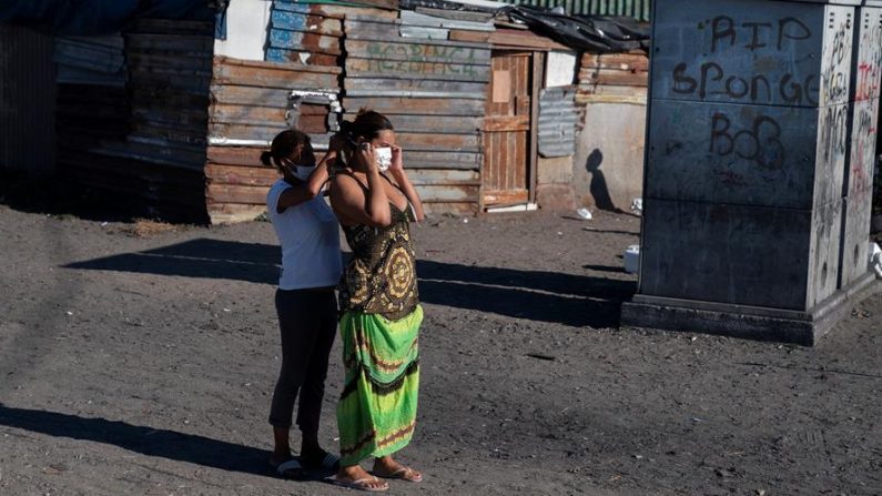 Una mujer sudafricana recibe ayuda mientras se pone una mascarilla facial protectora en el asentamiento informal de Masincedane, que es beneficiario del plan de alimentación COVID-19 del Proyecto 9 Millas y Esperanza del África Meridional (HOSA) en Ciudad del Cabo (Sudáfrica), 28 de abril de 2020. (EFE/EPA/NIC BOTHMA)