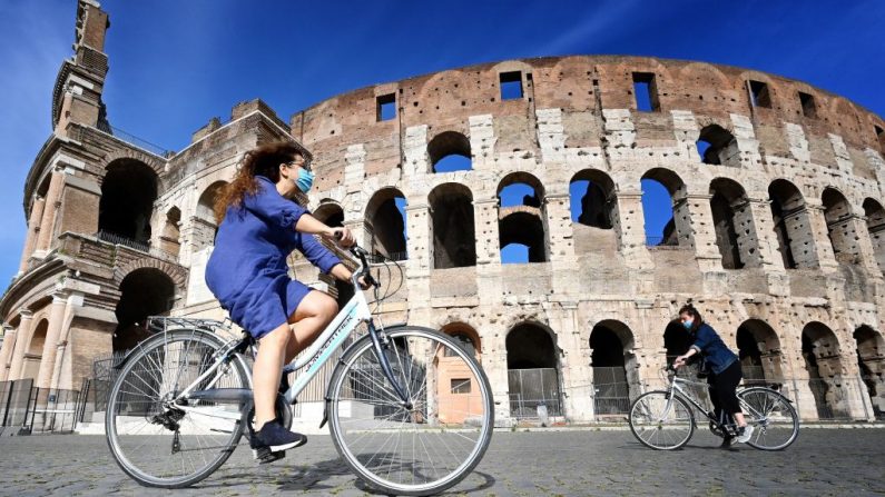 Mujeres pasan en bicicleta por el monumento del Coliseo de Roma (Italia) el 8 de mayo de 2020, durante el cierre del país para frenar la propagación de la infección COVID-19, causada por el virus del PCCh. (ALBERTO PIZZOLI/AFP vía Getty Images)