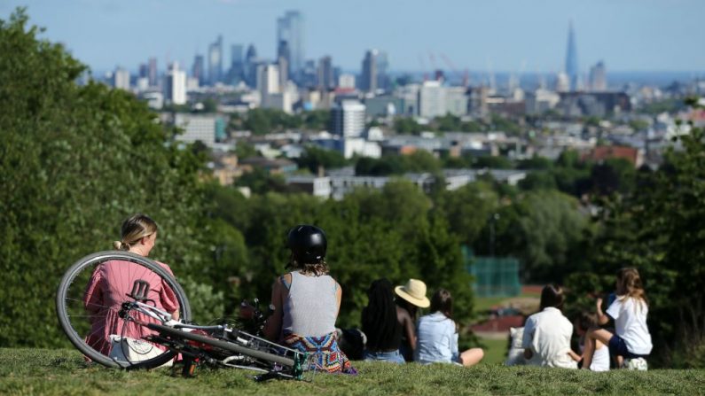 La gente toma el sol de la tarde en Hampstead Heath, al norte de Londres (Inglaterra), con el horizonte de la Ciudad de Londres, el 19 de mayo de 2020, después de la relajación de las restricciones de cierre impuestas debido a la pandemia de COVID-19. (ISABEL INFANTES/AFP vía Getty Images)