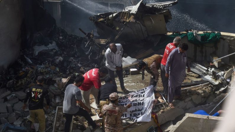 Trabajadores de rescate cubren el cuerpo de una víctima que recuperaron de los escombros después de que un vuelo de Pakistan International Airlines se estrellara en un barrio residencial de Karachi (Pakistán) el 22 de mayo de 2020. (ASIF HASSAN / AFP vía Getty Images)