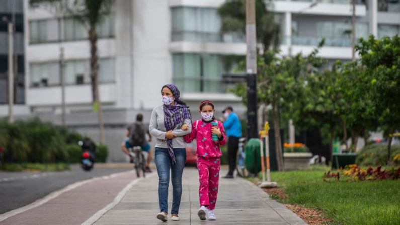 Una mujer camina con su hija con máscaras faciales en una calle de Lima (Perú) el 18 de mayo de 2020. (ERNESTO BENAVIDES/AFP vía Getty Images)