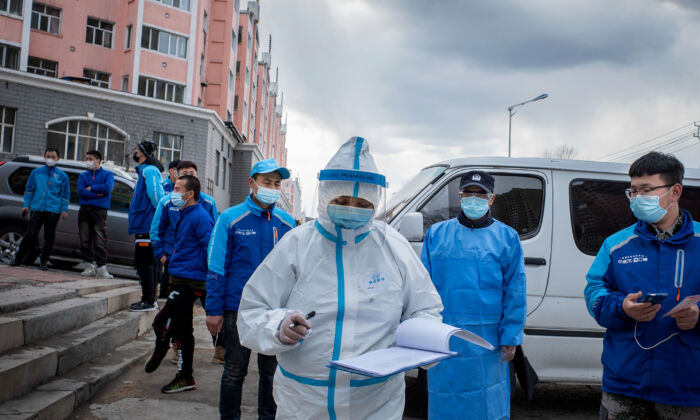 Un trabajador médico revisa algunas notas frente a los empleados de la entrega de alimentos, quienes esperan en fila para hacerse la prueba de ácido nucleico, en un centro de servicios de salud en Suifenhe, China, el 24 de abril de 2020. (STR/AFP vía Getty Images)