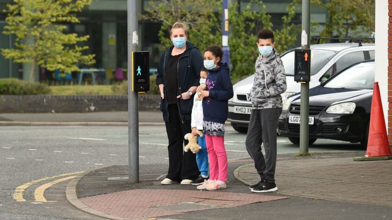 Las personas que usan máscara facial como medida de precaución contra el COVID-19, esperan para cruzar una carretera en Manchester, al noroeste de Inglaterra, el 1 de mayo de 2020. (OLI SCARFF/AFP vía Getty Images)