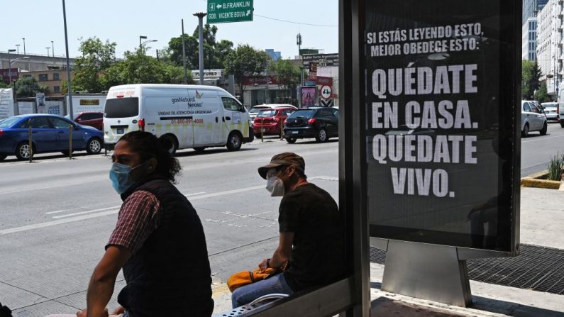 Los hombres esperan en una parada de autobús junto a un cartel que dice: "Si estás leyendo esto, mejor obedece esto: Quédate en casa. Quédate vivo" en la Ciudad de México (México), el 02 de mayo de 2020, en medio de la nueva pandemia del virus del PCCh. (RODRIGO ARANGUA/AFP vía Getty Images)