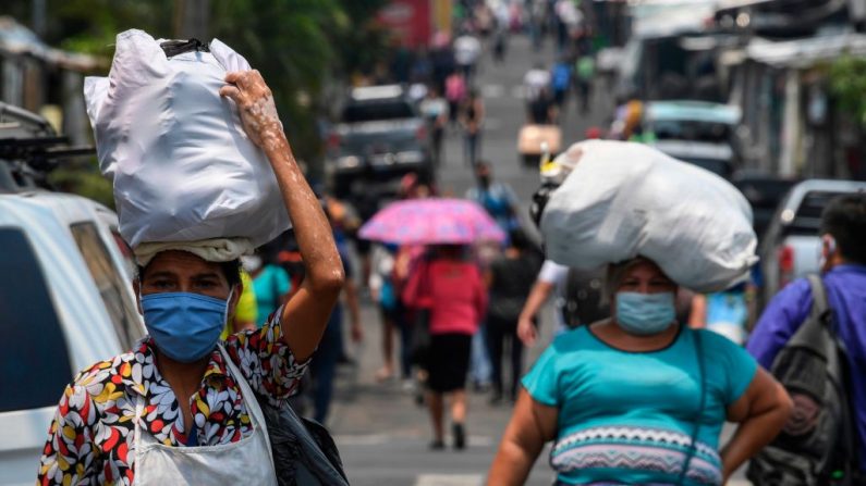 Las mujeres llevan sobre sus cabezas fardos de comestibles para enfrentar la cuarentena, después de haber asistido al mercado central de San Salvador (El Salvador) el 6 de mayo de 2020, en medio de la pandemia del virus del PCCh. (YURI CORTEZ/AFP vía Getty Images)