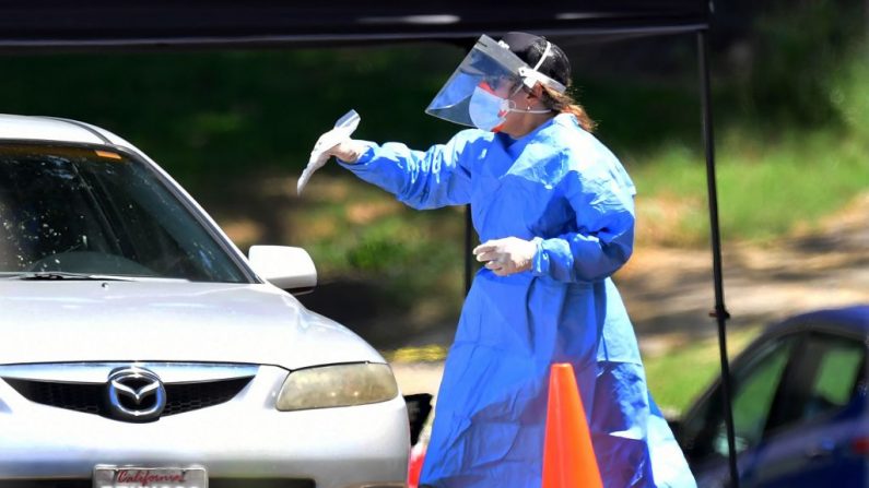 Una voluntaria sanitaria con equipo de protección entrega un novedoso kit de prueba de COVID-19 a un conductor en un lugar de pruebas móvil en Los Ángeles, California, el 6 de mayo de 2020. (FREDERIC J. BROWN/AFP vía Getty Images)