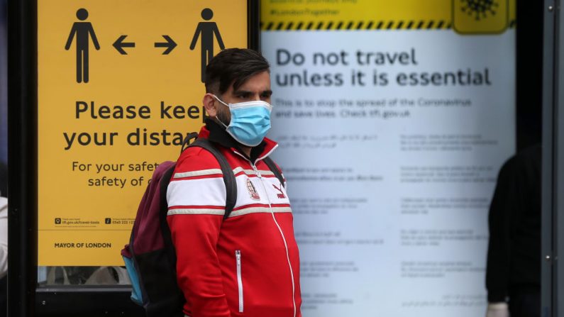 Un hombre con una máscara protectora espera en una parada de autobús rodeado de información sobre el distanciamiento social en Camden, en el centro de Londres, el 11 de mayo de 2020, mientras la vida en Gran Bretaña continúa durante el cierre nacional debido a la nueva pandemia del virus del PCCh. (ISABEL INFANTES/AFP vía Getty Images)