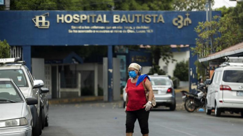Una mujer con tapabocas y guantes es vista mientras cruza la calle frente a un hospital privado en Managua (Nicaragua). EFE/Jorge Torres
