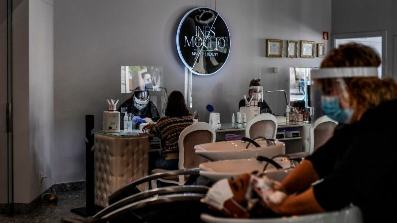 Estilistas con mascarillas faciales y escudos acrílicos atienden a clientes en un salón de belleza en Lisboa el 4 de mayo de 2020. (PATRICIA DE MELO MOREIRA/AFP vía Getty Images)