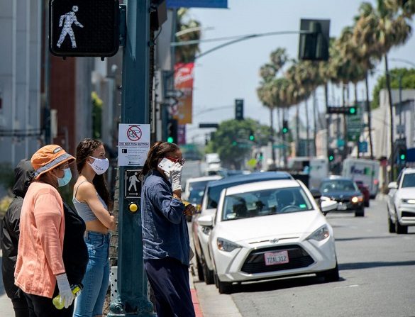 La gente espera para cruzar la calle en Rodeo Drive, donde se muestra un cartel pidiendo al peatón que no presione el botón, en medio de la pandemia de COVID- 19 en Beverly Hills, California, el 26 de mayo de 2020 (Valerie Macon/AFP vía Getty Images)