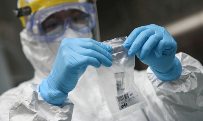 Un miembro del personal médico recoge una muestra en una escuela secundaria mientras los estudiantes reciben una prueba de ácido nucleico para el virus del PCCh en Guangzhou, China, el 21 de abril de 2020. (STR/AFP vía Getty Images)