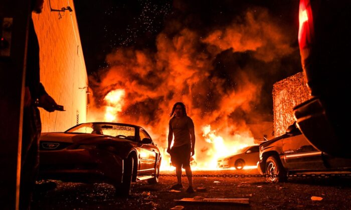 Un hombre intenta remolcar un coche en una zona segura mientras el otro coche se incendia en un aparcamiento local en Minneapolis, Minn., el 29 de mayo de 2020. (Chandan Khanna/AFP/Getty Images)