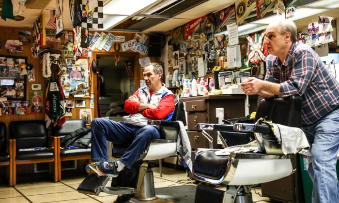 Los barberos y hermanos Tommy y Jimmy Checkler ven las últimas noticias sobre el virus del PCCh en su barbería vacía de la ciudad de Worthington en Columbus, Ohio, el 17 de marzo de 2020. (Charlotte Cuthbertson/The Epoch Times)