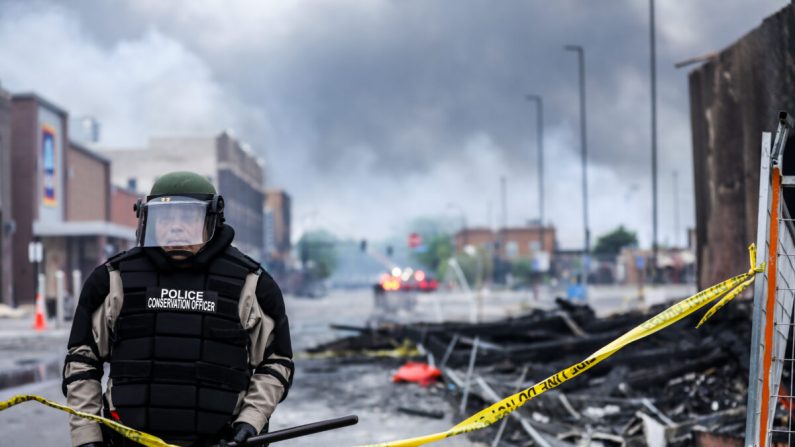 Un oficial de policía está de pie entre el humo y los escombros mientras los edificios siguen ardiendo tras una noche de protestas y violencia después de la muerte de George Floyd, en Minneapolis, Minnesota, el 29 de mayo de 2020. (Charlotte Cuthbertson/The Epoch Times)