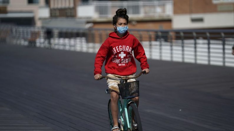 Una niña con una mascarilla anda en bicicleta por el paseo marítimo de Long Beach, Nueva York, mientras la gente comienza el fin de semana del Día de la Recordación el 22 de mayo de 2020. (Timothy A. Clary / AFP a través de Getty Images)
