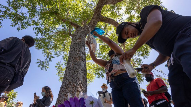 Una mujer sujeta globos y un hombre enciende velas en el árbol que las autoridades dicen que Robert Fuller, un hombre negro de 24 años, fue encontrado colgado muerto cerca del Ayuntamiento de Palmdale el 13 de junio de 2020 en Palmdale, California. (David McNew/Getty Images)