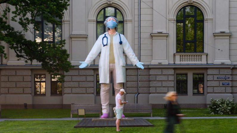Una mujer en un scooter pasa por delante de una estatua de 6 metros de altura de una doctora, del artista letón Aigars Bikse, llamada "Médicos para el mundo" ("Medi?i Pasaulei"), ubicada frente al Museo Nacional de Arte, el 17 de junio de 2020 en Riga (Letonia). (Gints Ivuskans / AFP a través de Getty Images)