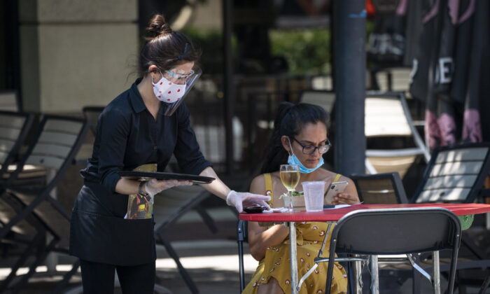 Una camarera de Raku, un restaurante asiático de Bethesda, lleva una mascarilla protectora para atender a los clientes al aire libre durante la pandemia de virus del PCCh en Bethesda, Maryland, el 12 de junio de 2020. (Sarah Silbiger/Getty Images)