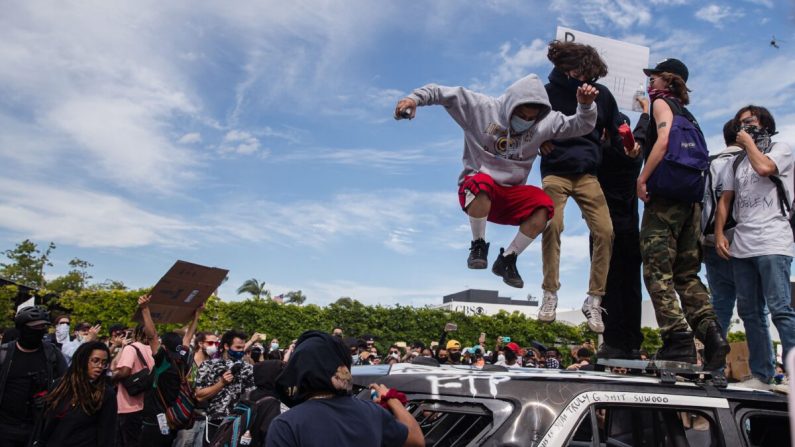 Los alborotadores saltan sobre un vehículo policial dañado en Los Ángeles el 30 de mayo de 2020 durante un disturbio contra la muerte de George Floyd. (Ariana Drehsler/AFP a través de Getty Images)