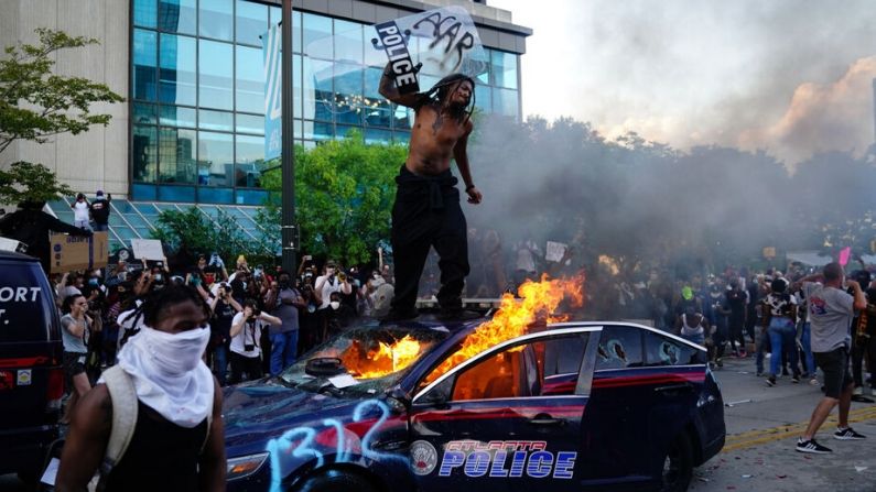 Un hombre parado sobre un auto de policía en llamas durante una protesta el 29 de mayo de 2020 en Atlanta, Georgia. (Elijah Nouvelage/Getty Images)