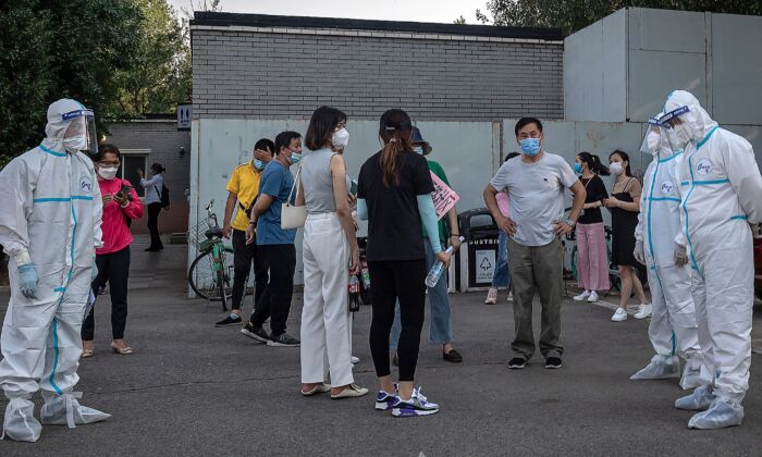 Los trabajadores que usan equipo de protección personal (EPP) cuidan a un grupo de personas que usan mascarillas faciales mientras esperan someterse a pruebas de coronavirus COVID-19 en Beijing, China el 19 de junio de 2020. (NICOLAS ASFOURI / AFP a través de Getty Images)