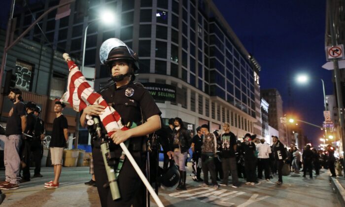 En esta fotografía se pueden ver manifestantes esposados tras el toque de queda mientras una policía lleva una bandera americana en Los Ángeles, California, el 2 de junio de 2020. (Mario Tama/Getty Images)