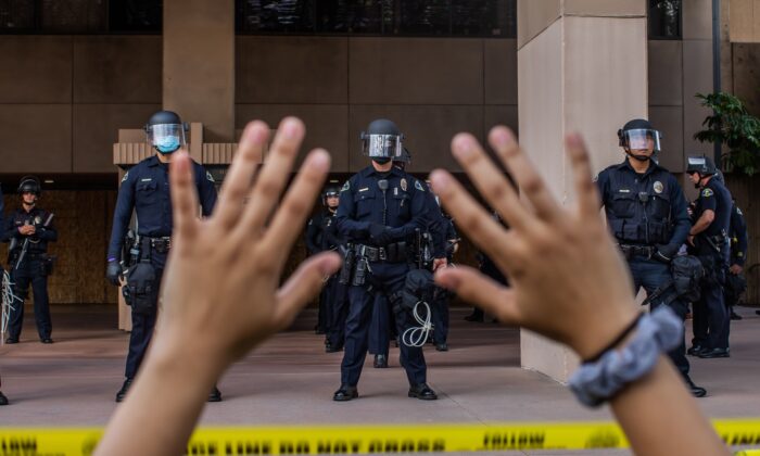 Una manifestante en una protesta por la muerte de George Floyd mantiene sus manos en alto mientras se arrodilla ante la policía en el Ayuntamiento de Anaheim, California, el 1 de junio de 2020. (Apu Gomes/AFP vía Getty Images)