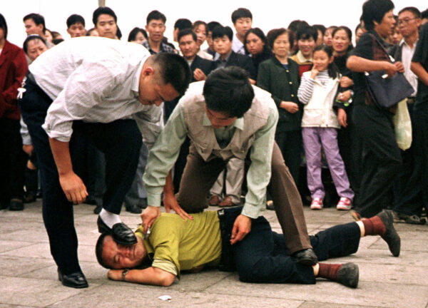 La policía detiene a un manifestante de Falun Gong en la Plaza Tiananmen mientras una multitud observa en Beijing la foto del 1 de octubre de 2000. (Foto AP / Chien-min Chung)