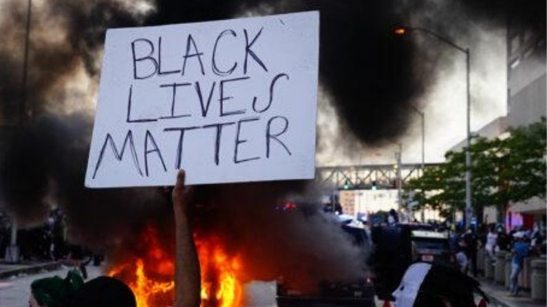 Un hombre sostiene un letrero de Black Lives Matter mientras un coche de policía se quema durante una protesta el 29 de mayo de 2020 en Atlanta, Georgia. (Elijah Nouvelage/Getty Images)