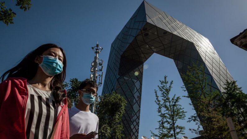 Personas con máscaras faciales pasan por el edificio de la sede de la Televisión Central de China (CCTV) y una torre de telefonía móvil, utilizada para una red 5G, en una calle de Beijing el 19 de mayo de 2020. (NICOLAS ASFOURI/AFP vía Getty Images)