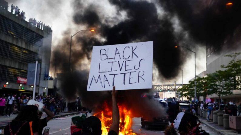 Un hombre sostiene un cartel de Black Lives Matter cuando un auto de la policía se quema durante una protesta en Atlanta, Georgia, el 29 de mayo de 2020. (Elijah Nouvelage/Getty Images)