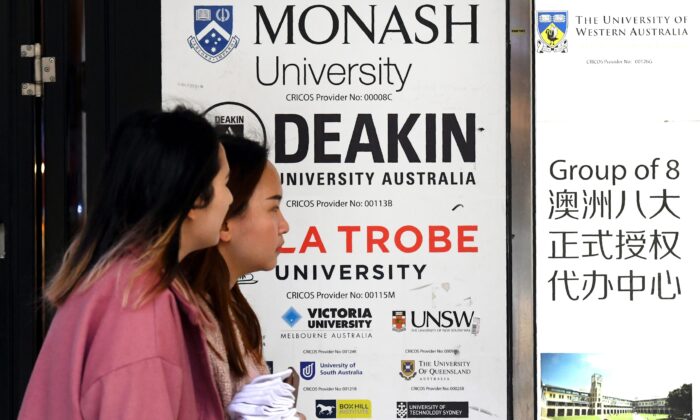 Dos chicas caminan frente a un cartel con los nombres de varias universidades de Australia en el distrito de negocios central de Melbourne el 10 de junio de 2020. (William West/AFP vía Getty Images)