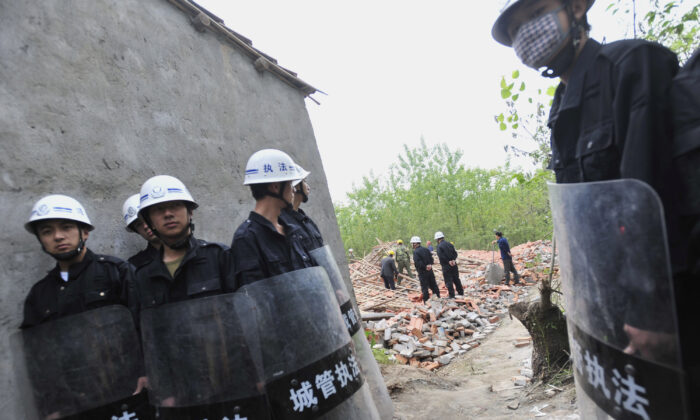 Agentes de seguridad chinos llevan palos durante su guardia mientras los trabajadores derriban casas en Wuhan, provincia de Hubei en el centro de China, el 7 de mayo de 2010. (AFP vía Getty Images)