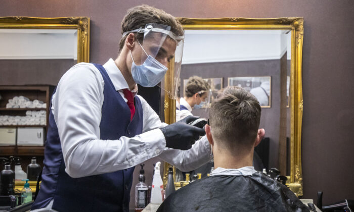 Un barbero con una máscara facial y un protector facial realiza un corte de pelo a un cliente en una barbería de Praga, República Checa, el 11 de mayo de 2020. (Gabriel Kuchta/Getty Images)