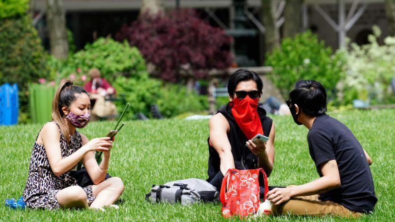 Tres personas usan mascarillas de protección mientras están sentadas en el césped del Parque Bryant en la ciudad de Nueva York, N.Y., el 22 de mayo de 2020. (Cindy Ord/Getty Images)