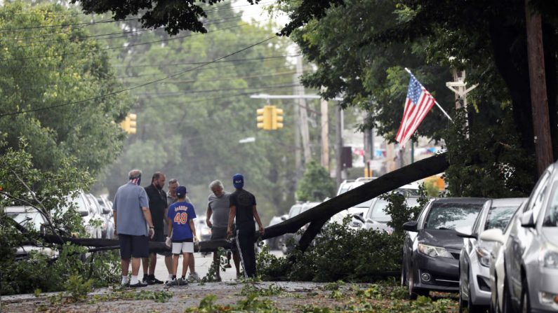 Los residentes tratan de mover un árbol caído que bloquea una carretera en un barrio de Brooklyn mientras la tormenta tropical Isaías se abre paso por la costa este el 4 de agosto de 2020 en la ciudad de Nueva York (EE.UU.). (Foto de Spencer Platt/Getty Images)