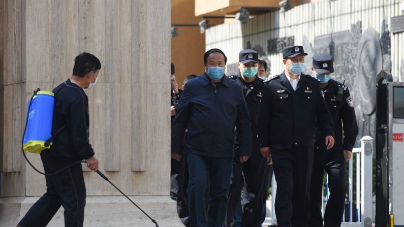 Funcionarios y policías salen de una escuela secundaria mientras un hombre (izq.) desinfecta la entrada del sitio, en Beijing, el 27 de abril de 2020. (Greg Baker/AFP a través de Getty Images)