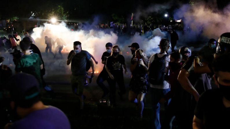 Los manifestantes corren para cubrirse mientras la policía dispara gase lacrimógeno en un intento por dispersar a la multitud fuera del Palacio de Justicia del Condado durante los disturbios por el tiroteo de Jacob Blake en Kenosha, Wisconsin, el 25 de agosto de 2020.  (Foto de KAMIL KRZACZYNSKI/AFP a través de Getty Images)