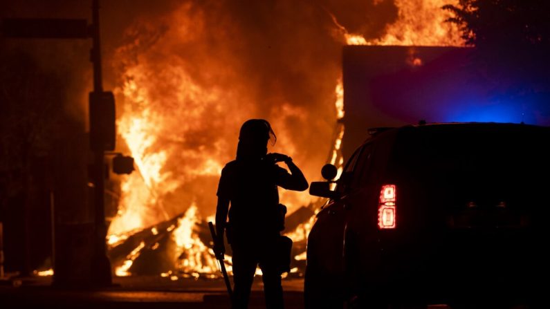 Un oficial de policía observa cómo una casa de empeño saqueada arde detrás de ellos, en Minneapolis, Minnesota, el 28 de mayo de 2020. (Stephen Maturen/Getty Images)