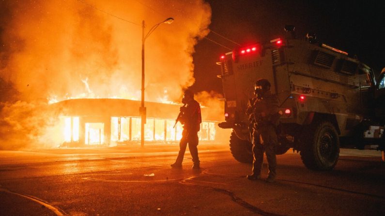 Un vehículo blindado de la policía patrulla una intersección mientras un edificio incendiado por alborotadores arde en Kenosha, Wisconsin, el 24 de agosto de 2020. (Brandon Bell/Getty Images)