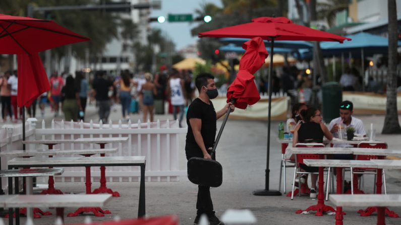 Un trabajador de un restaurante quita una sombrilla de la zona de asientos exteriores y se prepara para cerrar el restaurante por el día en Miami Beach, Florida (EE.UU.) el 18 de julio de 2020. (Foto de Joe Raedle/Getty Images)
