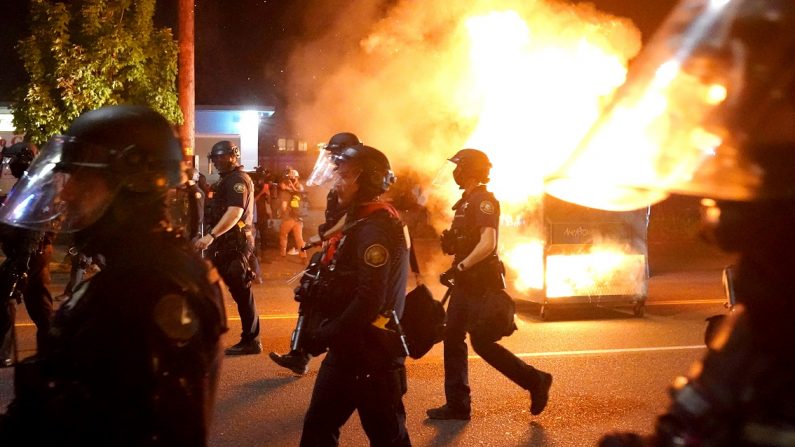 La policías pasan frente a un contenedor de basura en llamas durante la dispersión de una multitud en Portland, Oregón, el 14 de agosto de 2020. (Nathan Howard/Getty Images)